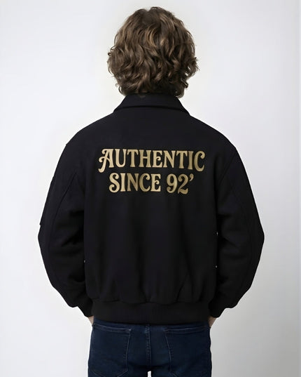 Person wearing a black jacket with 'AUTHENTIC SINCE 92' text on the back against a white background