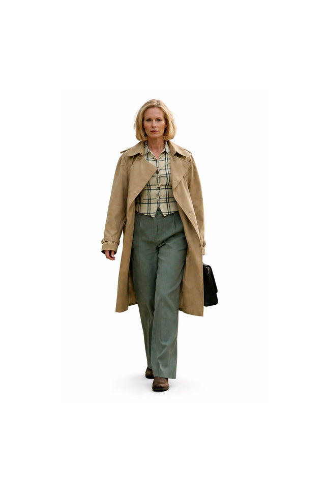 Woman wearing a beige trench coat and green pants on a white background