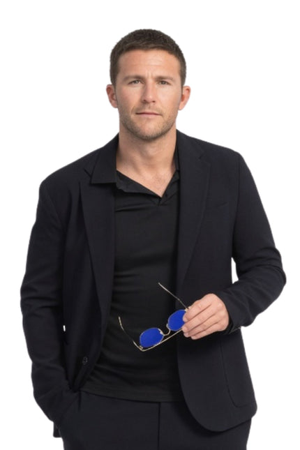 Man wearing a black suit holding blue sunglasses on a white background