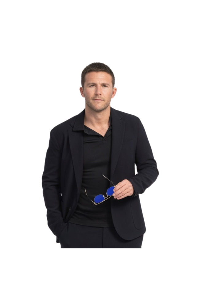 Man wearing a black suit holding blue sunglasses on a white background