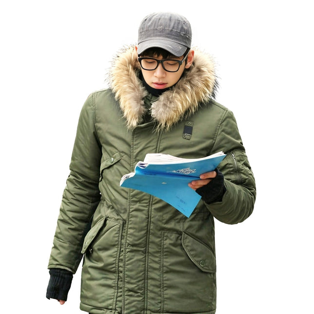 Person wearing a green winter coat with fur hood, holding blue papers on a white background