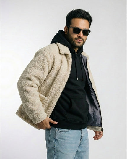 Man wearing a beige sherpa jacket over a black hoodie with sunglasses on a white background