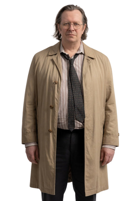 Man wearing a beige trench coat over a suit on a white background