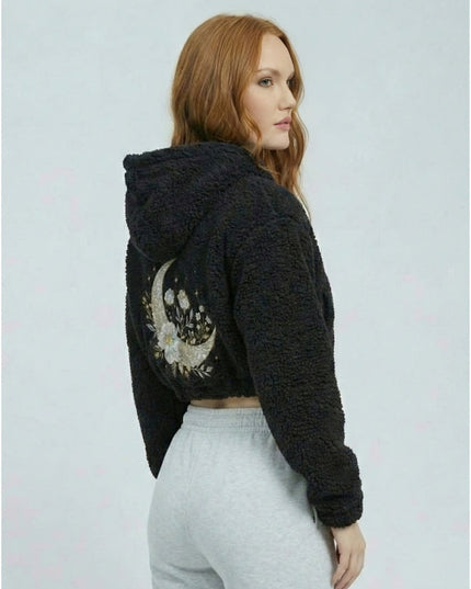 Woman wearing a black hoodie with a decorative back design on a light gray background