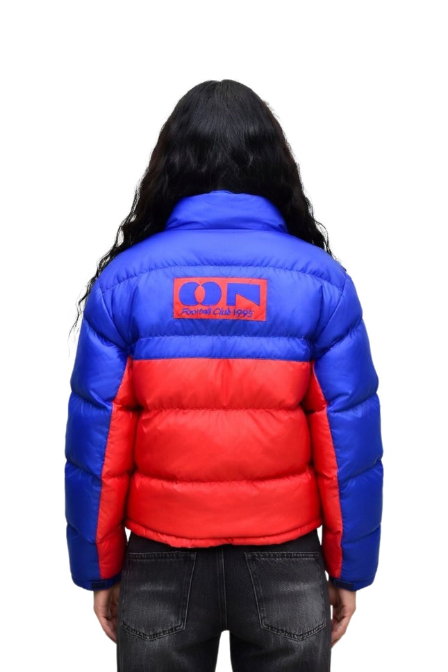 Person wearing a blue and red puffer jacket with a logo on the back against a white background