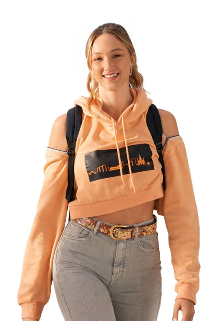 Woman wearing a peach hoodie with a graphic design, gray jeans, and a black backpack on a white background