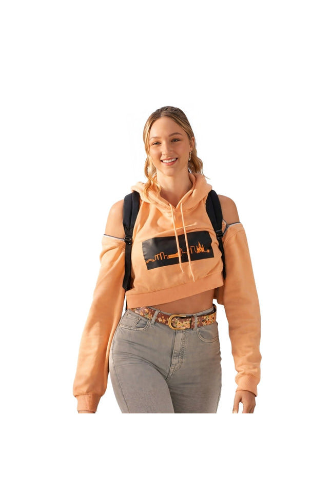 Woman wearing a peach hoodie with a graphic design, gray jeans, and a black backpack on a white background