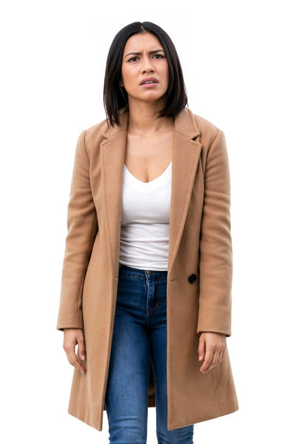 Woman wearing a tan coat over a white shirt and blue jeans on a white background