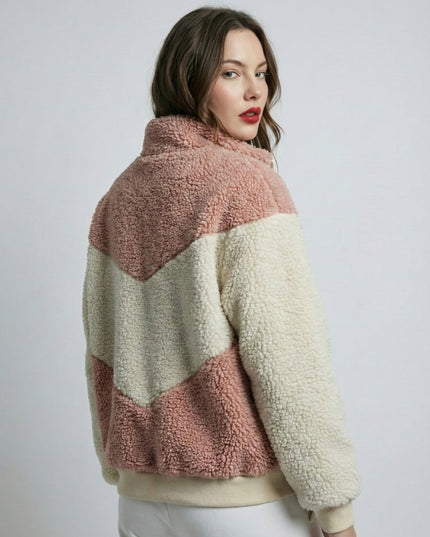 Woman wearing a two-tone sherpa jacket with pink and beige colors on a plain background