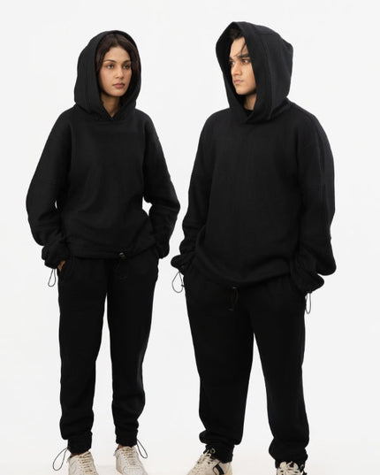 Two people wearing black hoodies and pants on a white background