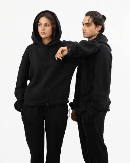 Two people wearing black hoodies and pants on a white background