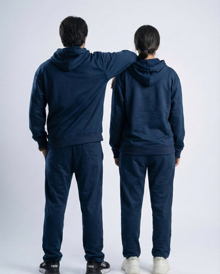 Two people wearing matching navy blue tracksuits standing back-to-back on a white background