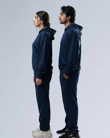Two people wearing navy blue tracksuits standing back-to-back on a light gray background