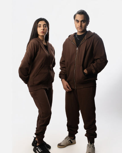 Two people wearing matching brown tracksuits on a white background