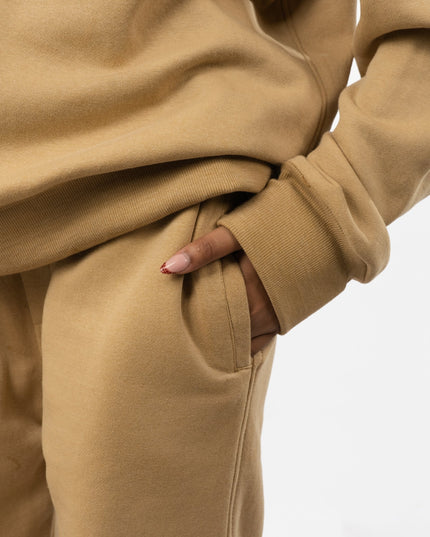 Close-up of a person wearing a beige tracksuit with hands in pockets on a light gray background