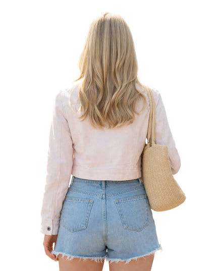 Woman wearing a light pink jacket and denim shorts, holding a beige bag on a white background