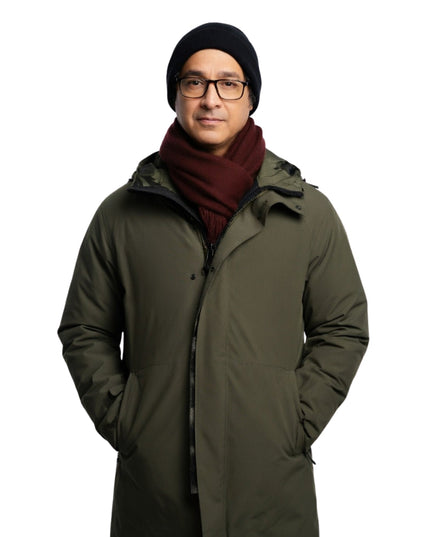 Man wearing a long green coat, black beanie, and glasses on a white background