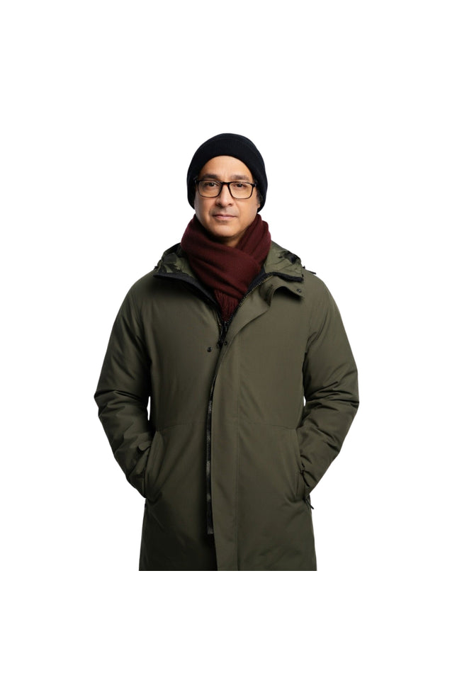Man wearing a long green coat, black beanie, and glasses on a white background