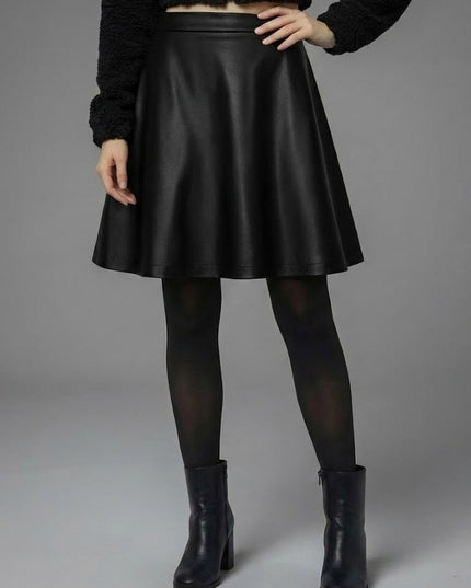 Person wearing a black leather skirt with black tights and boots on a gray background