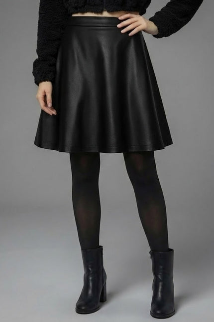 Person wearing a black leather skirt with black tights and boots on a gray background