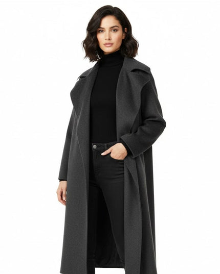 Woman wearing a long dark gray coat over a black outfit on a white background