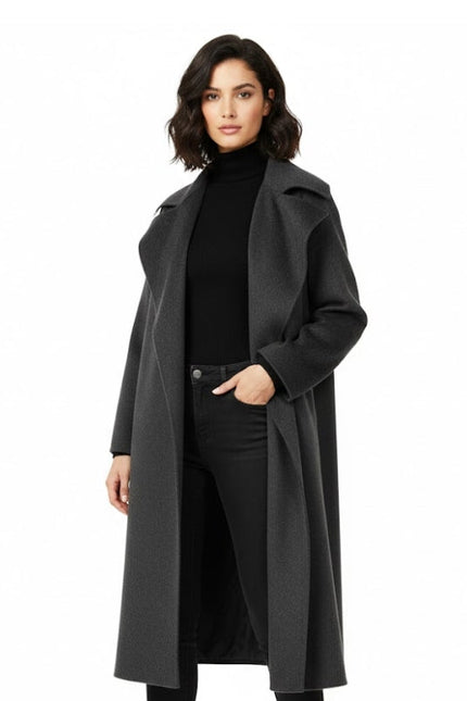 Woman wearing a long dark gray coat over a black outfit on a white background