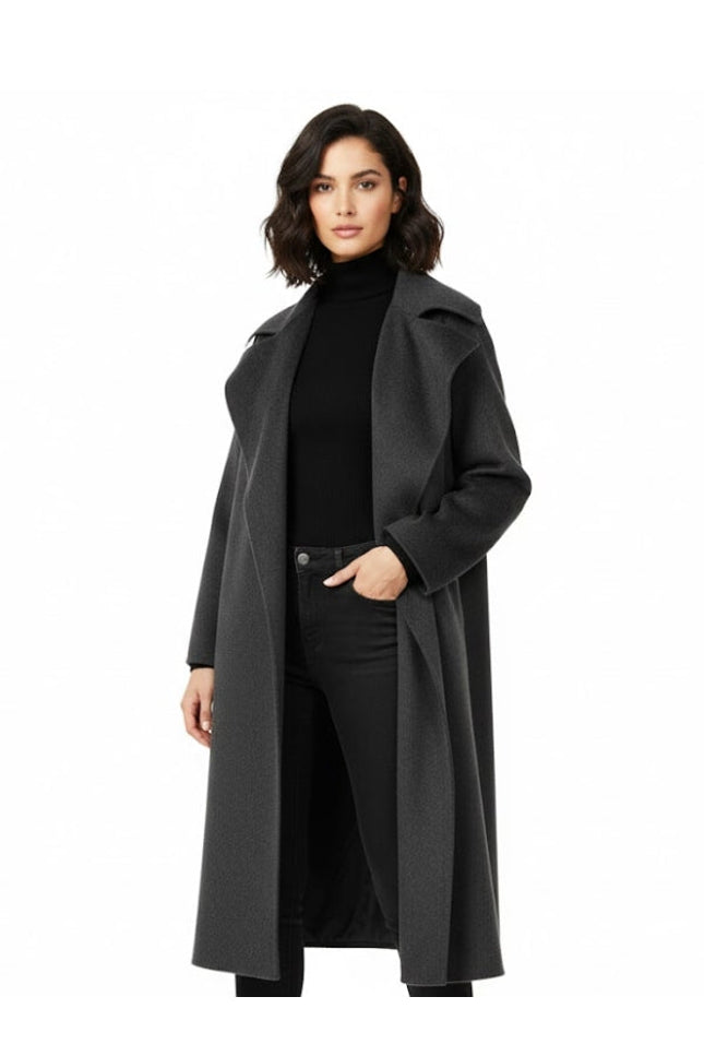Woman wearing a long dark gray coat over a black outfit on a white background