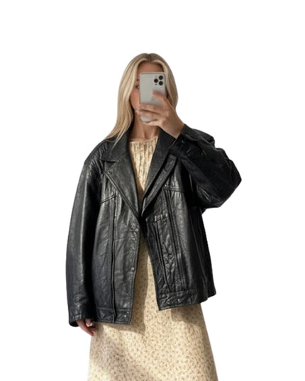 Person wearing a black leather jacket taking a mirror selfie on a white background