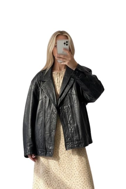 Person wearing a black leather jacket taking a mirror selfie on a white background