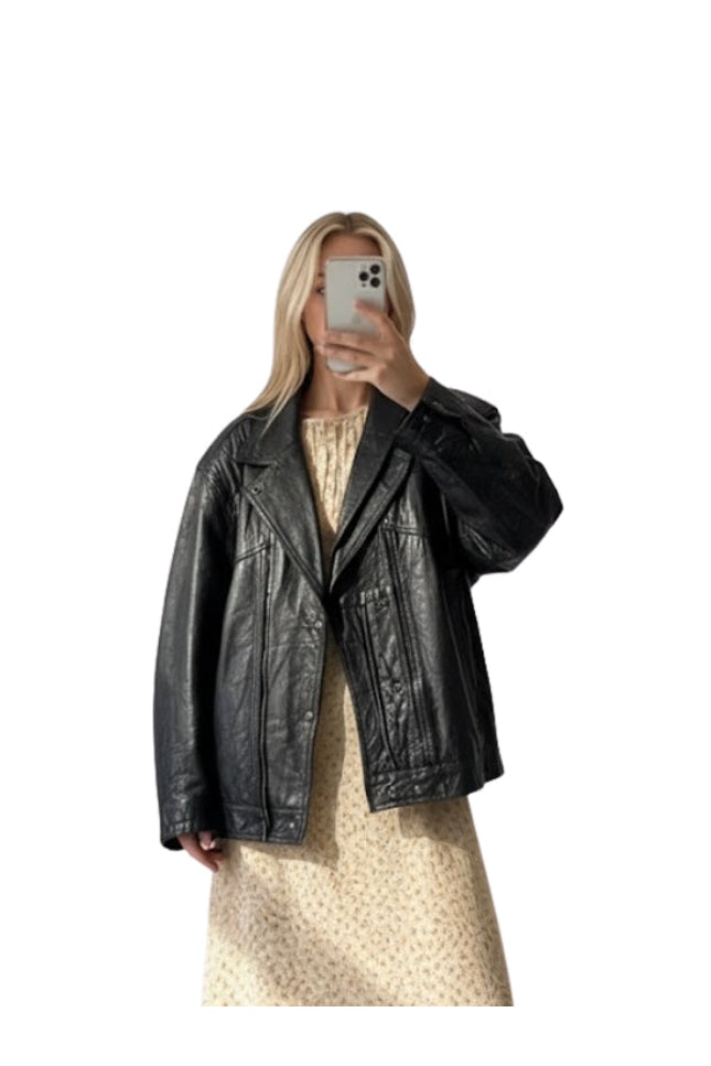 Person wearing a black leather jacket taking a mirror selfie on a white background