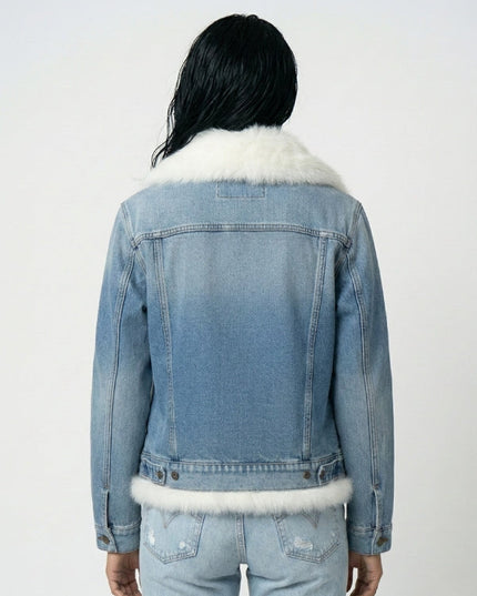 Person wearing a denim jacket with white fur trim on a plain background