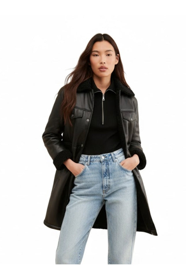 Woman wearing a black leather coat, black top, and light blue jeans on a white background