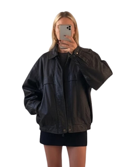 Person wearing a black jacket taking a mirror selfie on a white background