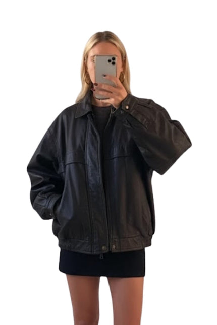 Person wearing a black jacket taking a mirror selfie on a white background