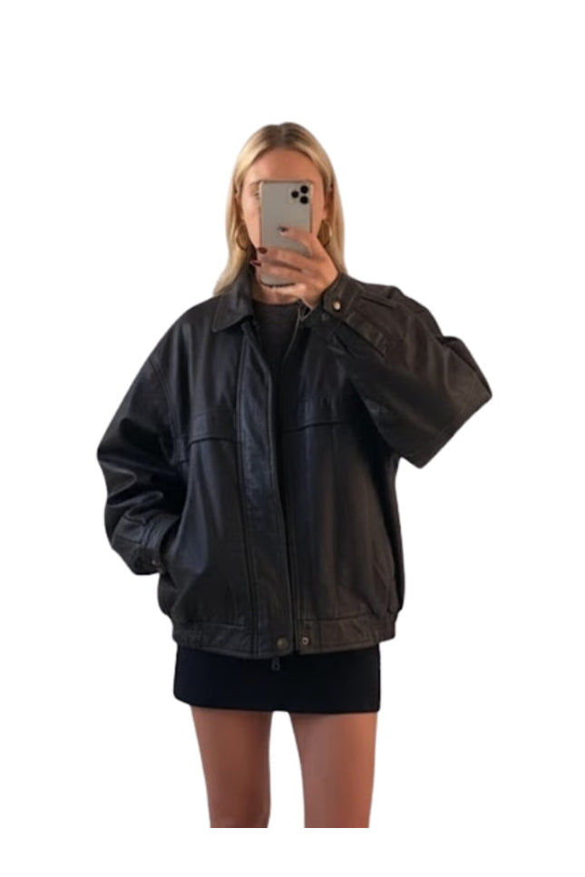 Person wearing a black jacket taking a mirror selfie on a white background